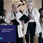 A diverse group of six healthcare professionals in white coats walk together down a hospital corridor, smiling and conversing. A banner overlay reads: "Modern Healthcare 2025 Largest Executive Search Firms – #8 DSG Global."