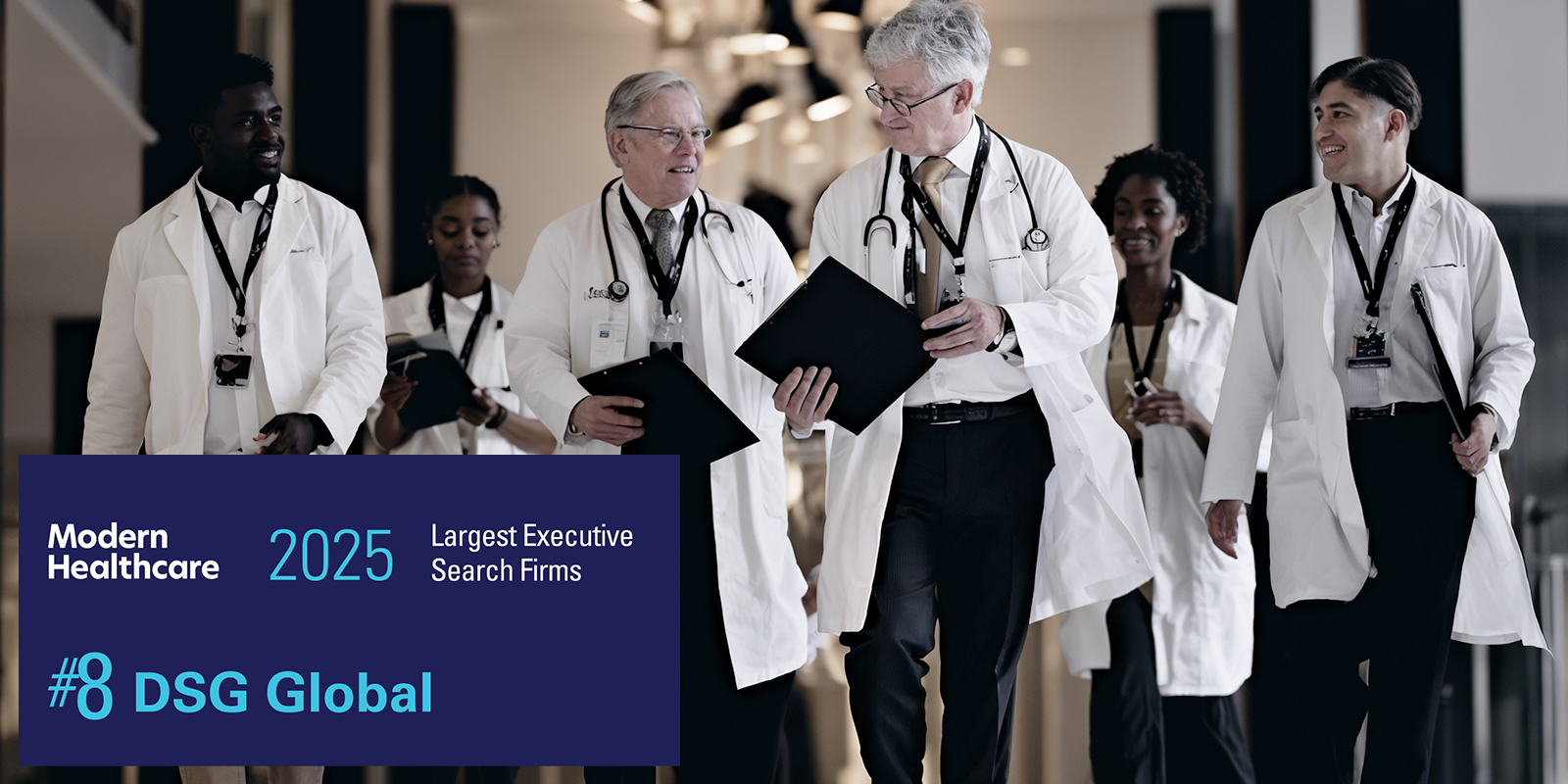 A diverse group of six healthcare professionals in white coats walk together down a hospital corridor, smiling and conversing. A banner overlay reads: "Modern Healthcare 2025 Largest Executive Search Firms – #8 DSG Global."